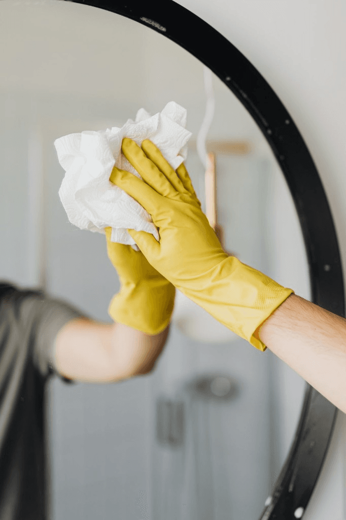 Gloved hand wiping a bathroom mirror clean